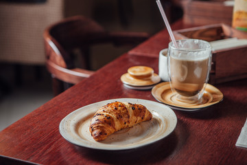 Croissant dusted with chocolate chips and a glass cup with cocoa on a dark wood table in the bar
