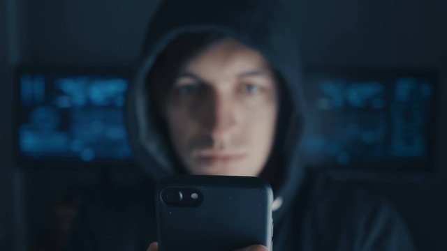 Crime Hacker in hood writing message on cell phone