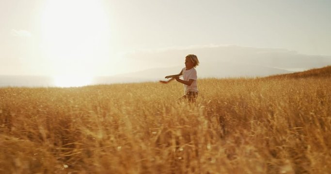 Adorable young boy running through golden field holding wooden airplane