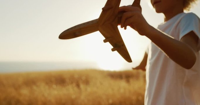 Happy young boy flying his wooden toy airplane in golden field at sunset