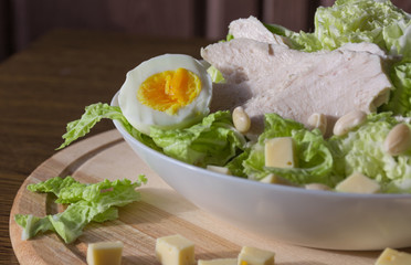 Food photography concept - plate of salad with boiled chicken meat, cheese, green salad leaves and eggs on wooden background