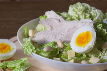 Food photography concept - plate of salad with boiled chicken meat, cheese, green salad leaves and eggs on wooden background