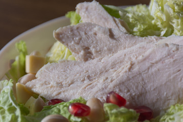 Food photography concept - close up of plate of salad with boiled chicken meat, cheese, green salad leaves on wooden background