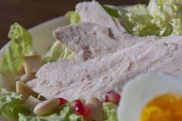 Food photography concept - close up of plate of salad with boiled chicken meat, cheese, green salad leaves on wooden background