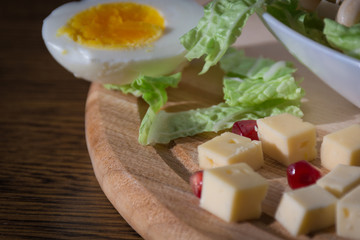 Food photography concept - plate of salad with boiled chicken meat, cheese, green salad leaves and eggs on wooden background