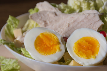Food photography concept - plate of salad with boiled chicken meat, cheese, green salad leaves and eggs on wooden background