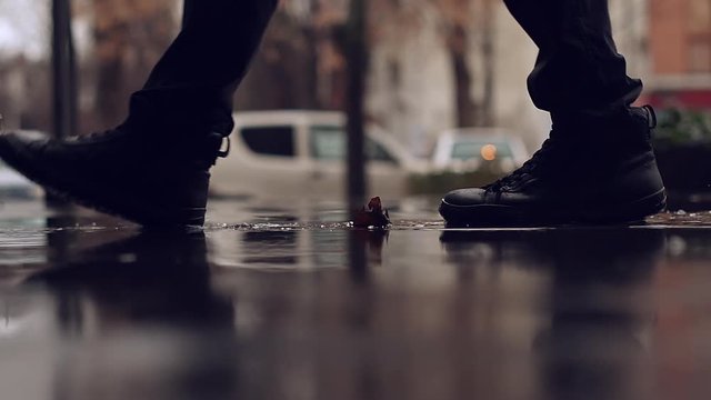 Walking through rain puddle, low angle view of male feet in boots stepping into water on the pavement on a rainy autumn day, slow motion