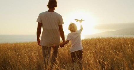 Adorable father and son walking together through golden field at sunset