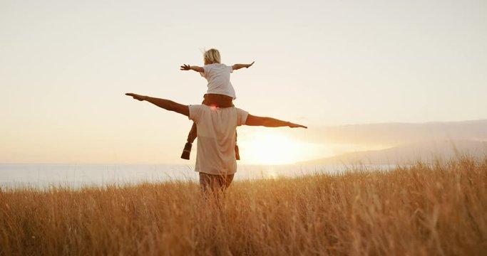 Adorable father and son playing airplane together, walking in golden field at sunset