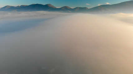 Panoramic aerial view of countryside scenario surrounded by fog, view from drone above the clouds