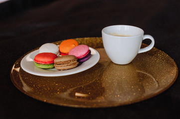 A cup of tea is on the table next to the plate in which the multi-colored cookies
