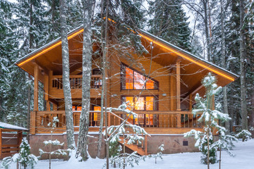 Snow-covered beautiful wooden house in the forest at dusk