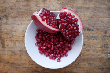 sliced pomegranate and pomegranate fruits in a white plate on a wooden dark background
