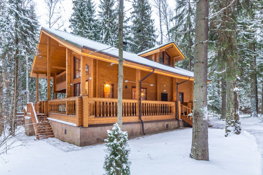 Snow-covered beautiful wooden house in the forest at dusk. Modern log cabin with large decks
