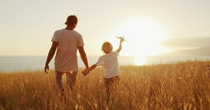 Adorable father and son walking together through golden field at sunset