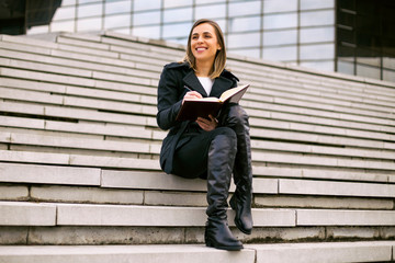 Beautiful businesswoman sitting on the staircase in the city and working.