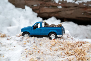 Obraz premium Blue toy pickup truck in sawmill. Stuck at snowdrift and sawdust. Carrying fir cones in the back of a car body.
