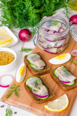 Open sandwich with rye bread, fresh cucumber, pickled onions, herring and dill on a wooden board
