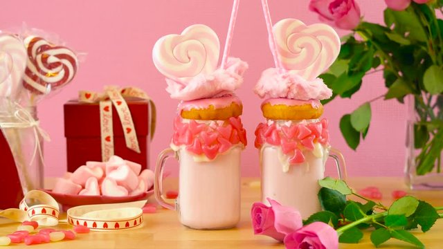 4k On-trend Valentine's Day table setting with pink strawberry freak shakes topped with heart shaped lollipops, donuts and cotton candy.