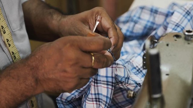close view tailor hands cut wrong line with special tool sitting at sewing machine in small workshop corner 
