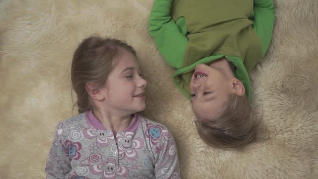 Cute little kids in pajamas lying on the floor with fluffy carpet. Brother and sister have a fun together. Happy siblings weekend.