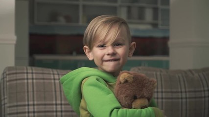 Portrait of a little cute cheerful boy in pajamas hugging a teddy bear standing in the living room. Happy joyful child. Slow motion.