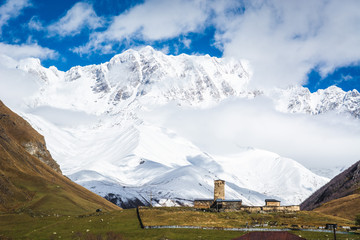 Picturesque landscape of aged Georgian rural community Ushguli and LaMaria church in valley of beautiful mountains with snowy peaks, Mt. Shkhara, the highest peak of Georgia on the background, Svaneti