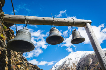 Bells in Lamaria church in Zhibiani - Ushguli community of villages, Upper Svaneti, Georgia. Snow covered peak of Shkhara mountain on background