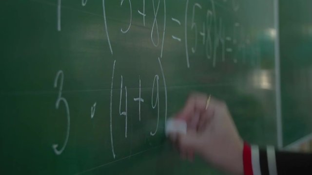teacher's hand writing maths assignment on green chalkboard for pupils in school on Math lesson