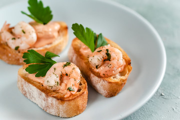 Bruschetta sandwiches with shrimps, creamy sauce and parsley.