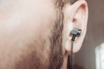 Bearded man with earphone in the ear close up.