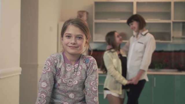 Portrait of a happily smiling little girl on the background of two embracing older sisters. Family relationships