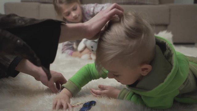 Two cute kids laying on the floor on the fluffy carpet playing their toys at home. Male hand stroking a playing child. Happy kids weekend.