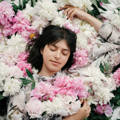 Beautiful brunette girl in many pink and white peonies. Happy boho woman portrait with peony flowers, top view. Creative floral photo. Aroma scent concept. International Womens Day