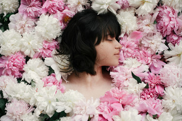 Portrait of boho woman with natural makeup lying in peonies. Creative floral photo. Aroma and spa concept. International Womens Day. Beautiful brunette girl in many pink and white flowers