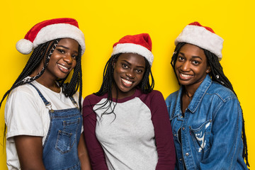 Portrait of young african women in santa hats isolated on yellow background