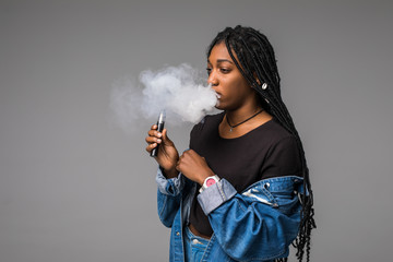 Portrait of guy holding vape device and exhaling cloud of smoke isolated on blue background.