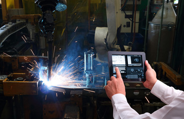 Industry 4.0 ,  concept  of Man hand holding cell phone or tablet with Augmented reality screen software and blue tone of automate wireless Robot arm in smart factory background. Mixed media