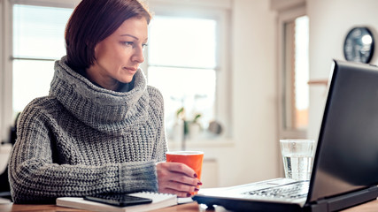 Woman using laptop and drinking coffee