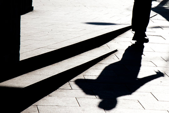 Blurry silhouette shadow of a man walking on a city sidewalk with steps  in black and white