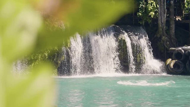 Young woman jumping in mountain lake from rope and splashing waterfall on background. Slow motion. Happy woman jumping in waterfall lake from rope and stick. Extreme rest on summer vacation.