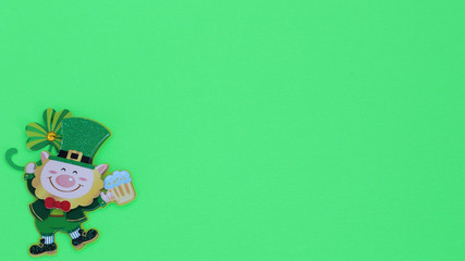 Leprechaun holding a beer mug laying flat on a green background with writing space