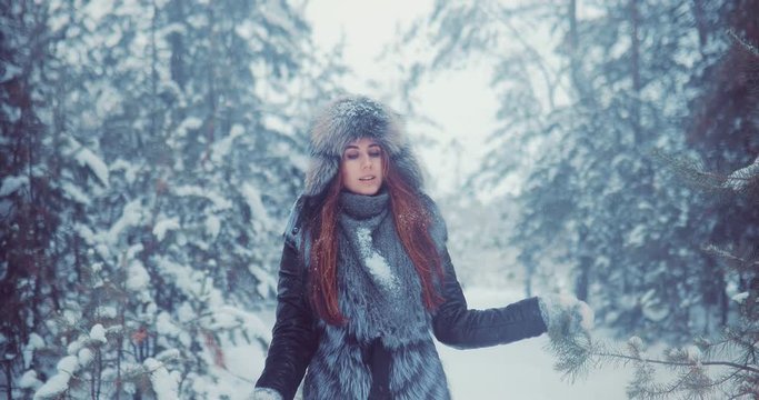Woman in a winter hat, jacket and mittens walks through a winter forest. Girl walks in the snow and touches tree branches.