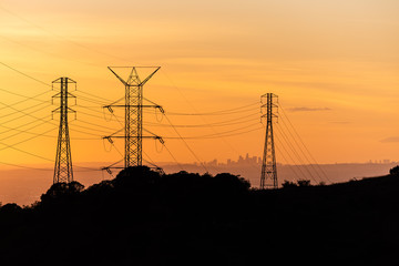 Silhoutte of Los Angeles skyline seen through power lines during a golden sunset.