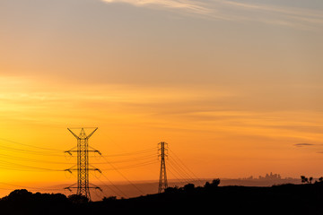 Silhoutte of Los Angeles skyline seen through power lines during a golden sunset.