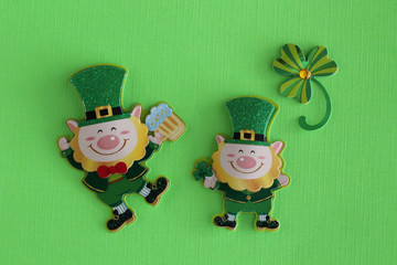 two leprechauns with a clover laying flat on a green background with writing space