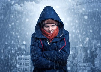 Young man freezing in warm clothing with city concept
