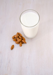a glass of milk next to nuts of almonds on a wooden table