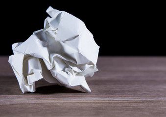 Crumpled paper lies on a table against a black background