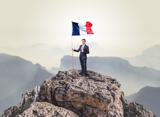Obraz premium Successful businessman on the top of a mountain holding France victory flag 